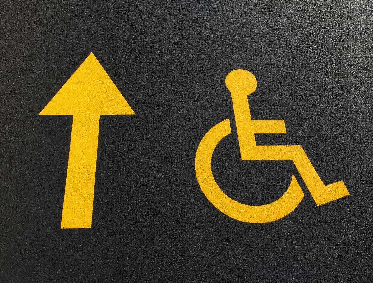 Freshly painted yellow directional arrow and ADA stencil on a parking lot